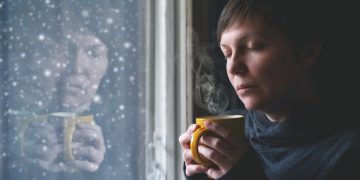 Woman sitting by a seasonal depression lamp with a fidget ring and cup of herbal tea for anxiety.