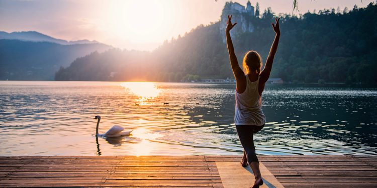 Person practicing yoga at sunrise on a dock, demonstrating calming strategies to manage anxiety with mindfulness and grounding techniques, like fidget rings