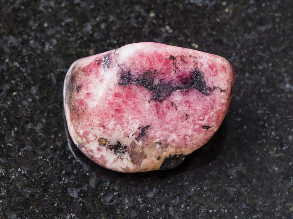closeup of sample of natural mineral from geological collection - tumbled Rhodonite gem isolated on white background